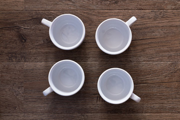 Food concept - top view of four white cups without saucers on gray brown wood table. Empty ceramic mugs.