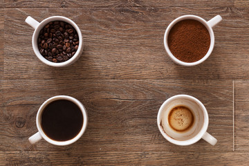Variety of cups of coffee and coffee beans on old wooden table. Four cups of coffee, phases of drink - bean, ground and empty cup.