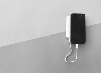 Closeup A black smartphone charging with a white powerbank set on Gray background.Gadgets on gray background.Top view with Copy space. Selective focus.