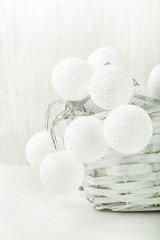 White Cotton Balls Garland in Wicker Basket. Christmas New Year Decoration. Wood Background. Scandinavian Style. Monochrome. Copy Space.