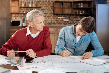 Senior man supervising young colleague drawing blueprint