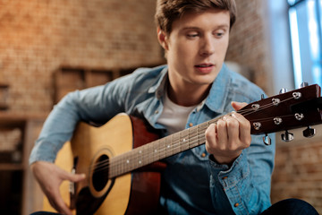 Pleasant young man playing guitar at home