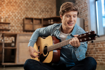 Obraz premium Cheerful young man playing guitar and smiling