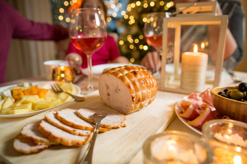 Happy family celebrating holiday together, sitting around decorated round table, food close-up. Living room with Christmas tree, lights and candles. Merry Christmas concept