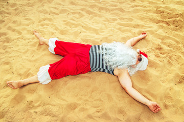 Santa Claus is liyng on the beach.