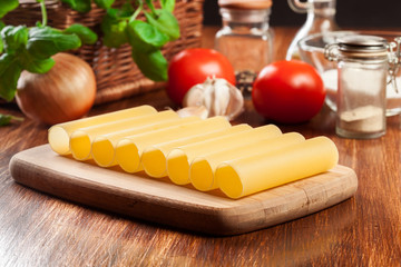 Uncooked cannelloni pasta on cutting board and ingredients