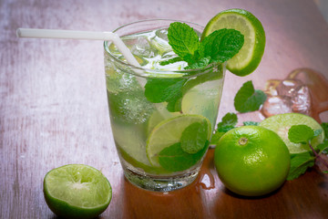 Fresh Mojito cocktail with fresh green limes, mint and ice on wooden background.