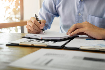 business men working on wooden desk(table) with notebook computer paper, pencil and hand in office, financial concept.