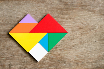 Colorful tangram puzzle in heart shape on wood background