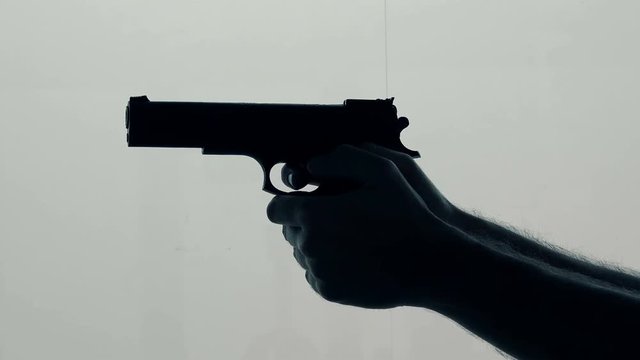 Hand with a gun shooting. Violence and crime with use of fire weapon, back lit silhouette