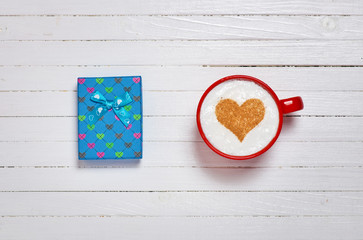 Cup of coffee with heart shape symbol and gift box on wooden white background