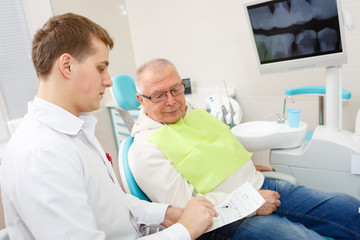 Elderly man on a review of a dentist, sitting in a chair. Focus on doctor