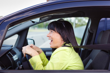 Scared and surprised woman with big eyes holds the steering wheel with both hands shouts driving the car - outdoors