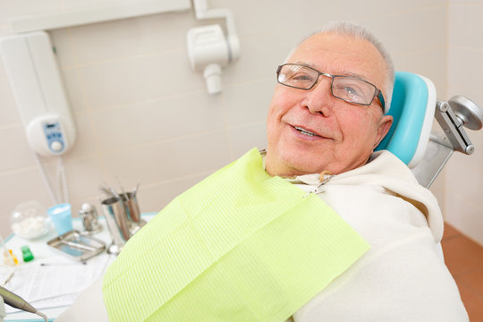 Old senior man with glasses sitting in a dental chair in a dentist's office.