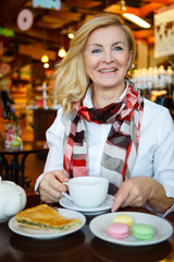 Portrait of smiling and happy old senior business woman sitting at table in cafe. Tea or coffee time and breakfast