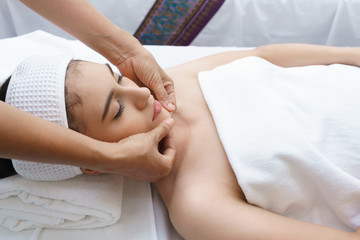 Beautiful young Asian woman relaxing , lying on massage table and having Thai traditional face massage in spa salon