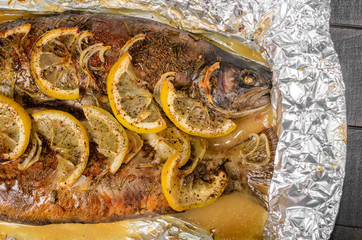 Baked trout, fish with spices, herbs and lemon in a baking dish top view