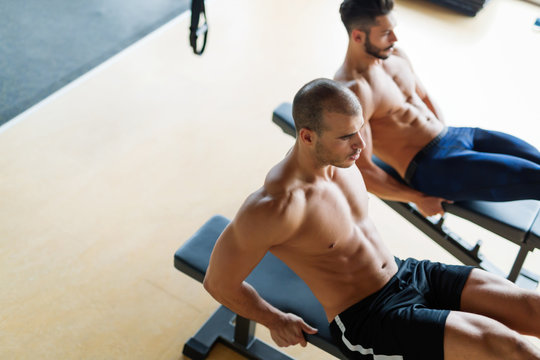 Strong men are doing abs crunches on bench