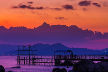 The coastal zone in the rays of a purple sunset. In the background, silhouettes of mountains are visible. End of the Earth. Hainan, China.