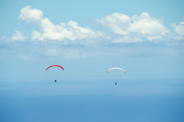 Red and white paragliders fly over Indian ocean with clouds at the background in Reunion island, France.