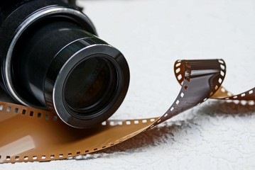 часть чёрного фотоаппарата с объективом и коричневой плёнки
