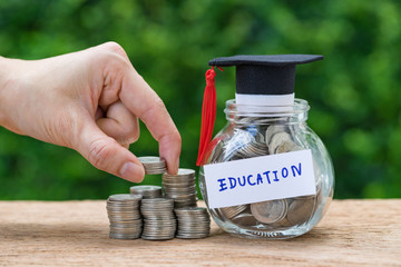 Woman hand holding stack of coins money and glass jar with full of coins and graduates hat label as...