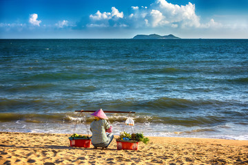 A saleswoman of fruit sits on the beach in front of the sea.