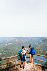 Fototapeta na wymiar Young tourists with backpacks enjoying the view from top of a mountain. Looking through binoculars 