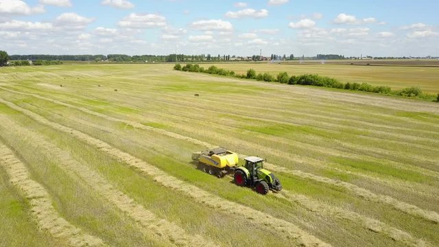 Ukraine, Kalinovka, September 4, 2017, Green tractor with Hay baler producing hay bales in a field - Aerial footage, summer, the sun is shining