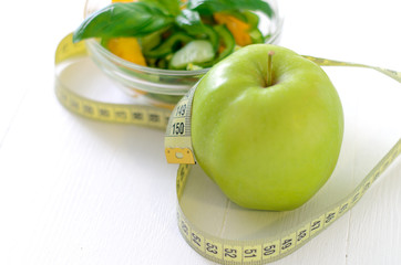 healthy eating, dieting, slimming and weigh loss concept - close up of green apple, measuring tape and salad