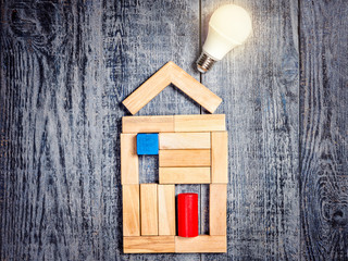 Form of house above tree on dark wooden background and LED bulb. Imitation of heating copper or...