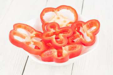 Heap of slices of red fresh ripe raw pepper in ceramic bowl on old rural white wooden planks