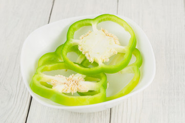 Heap of slices of green fresh ripe raw pepper in ceramic bowl on old rural white wooden planks