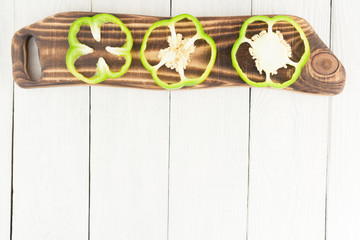 Row of slices of green fresh ripe raw pepper on brown cutting board on old rural white wooden planks