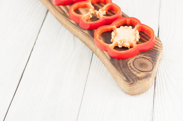Row of slices of red fresh ripe raw pepper on brown cutting board on old rural white wooden planks