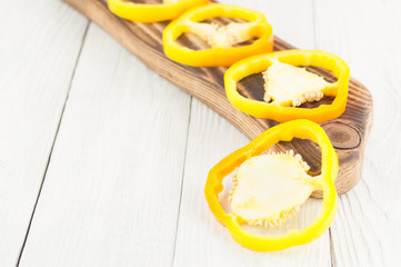 Row of slices of yellow fresh ripe raw pepper on brown cutting board on old rural white wooden planks