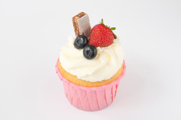 Pink cupcake with white whipped cream decorated with strawberry, blueberry, granola bar on white background. Picture for a menu or a confectionery catalog.