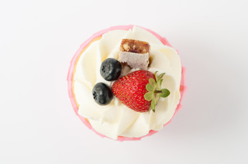 Pink cupcake with white whipped cream decorated with strawberry, blueberry, granola bar on white background. Picture for a menu or a confectionery catalog. Top view.