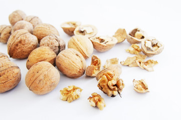 Walnut kernels in a wooden bowl and whole walnuts on a white background. Walnuts
