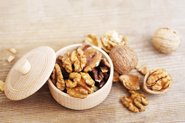 Walnut kernels in a wooden bowl and whole walnuts on old wooden table. Walnuts