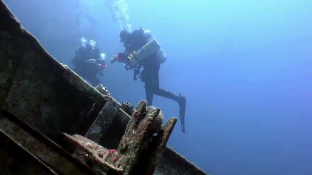 Scuba divers swimming explore shipwreck Salem Express deep underwater Red sea. Secret of sunken ship which crashed on coral reef. Historical place of tragedy.