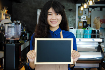 Fototapeta premium Portrait of asian barista holding blank chalkboard menu in coffee shop. Cafe restaurant service, Small business owner, food and drink industry concept.