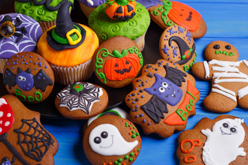Fototapeta na wymiar Halloween dessert: funny monsters, ghosts and pumpkins made of biscuits with confectionery mastic decorations on the table, close-up