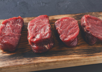 Raw beef filet mignon steaks on wooden board at gray background