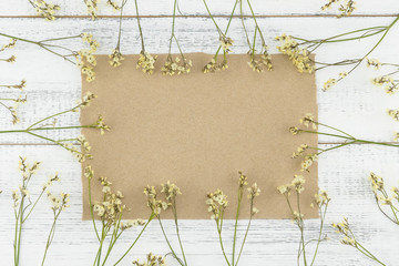 Blank brown card decorated with yellow limonium caspia flowers on white wood background 