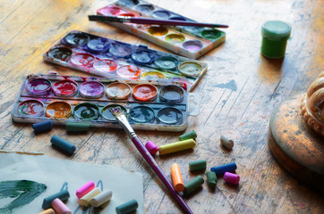 Old pastels crayons, three palettes of different colors, colorful paint tubes and artistic brush on...