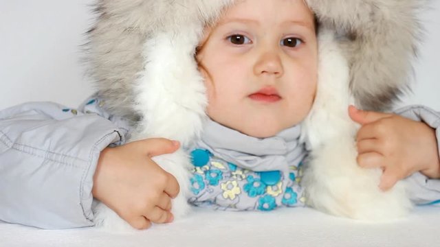 A funny child dressed in warm fur clothes and looking at the camera. Close-up portrait. The concept of winter, frost and snow, cold weather, cool temperature and Christmas.