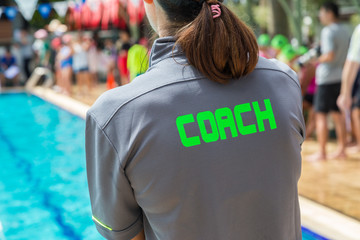 back of a swim coach's grey shirt with the green word Coach written on it