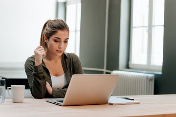 Portrait of young woman sitting at her work desk and looking at laptop.