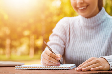 Close up of happy woman writing on paper on table in park.